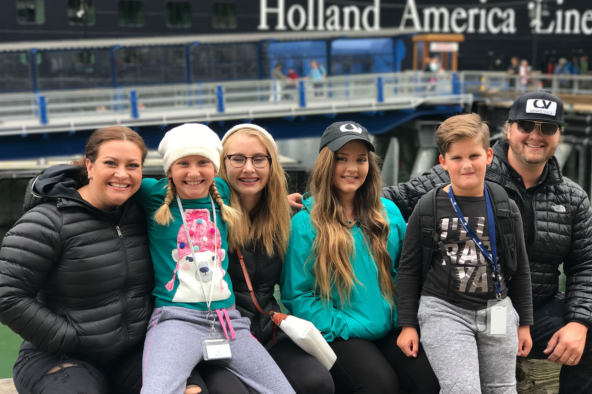 Family group photo with TaRanda wearing casual and warm clothes, seated at a harbor with a cruise ship in the background.