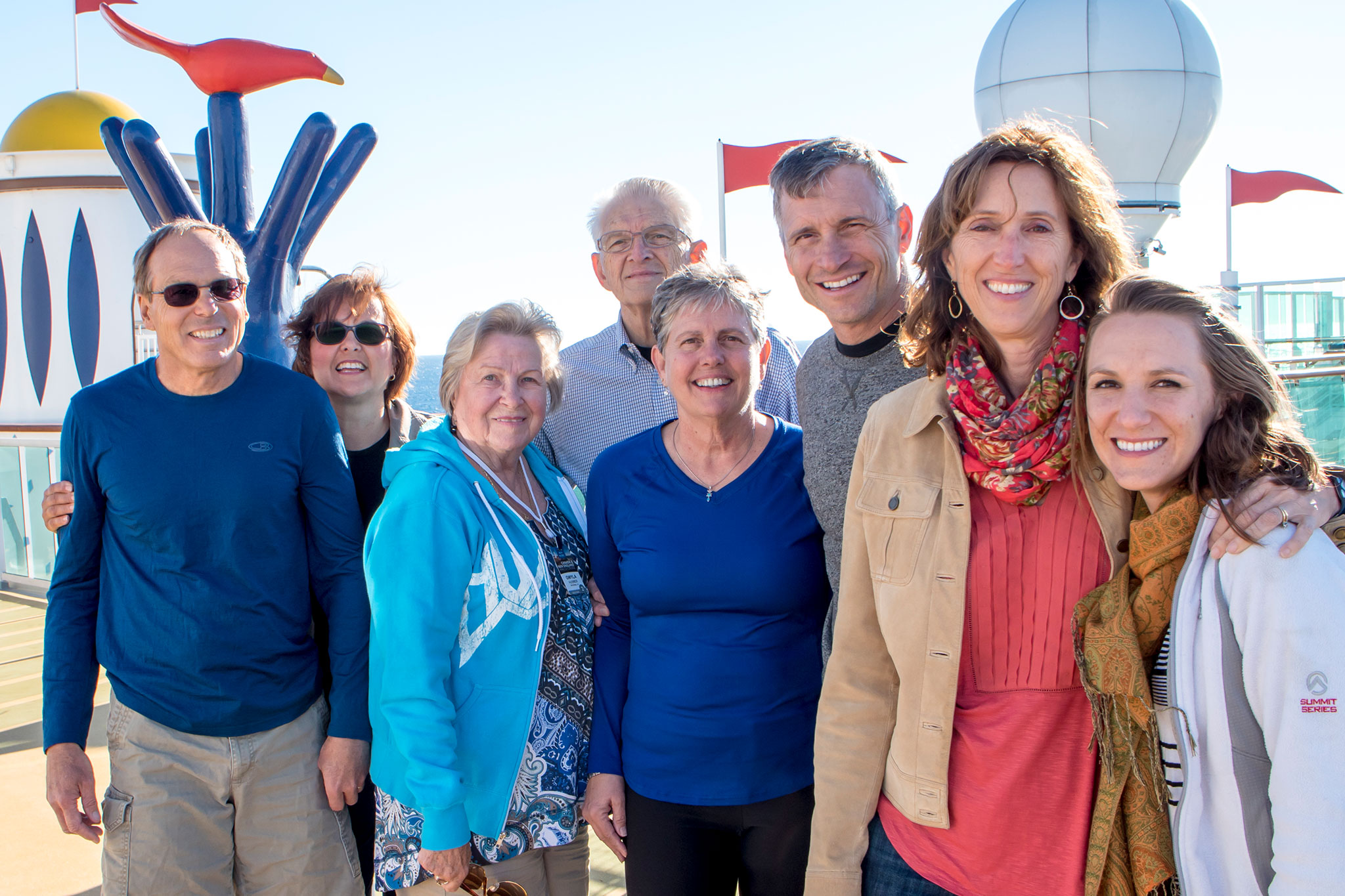 Happy multigenerational family enjoying a sunny day on a cruise ship deck, with a playful art installation and the ship's antenna visible behind them.