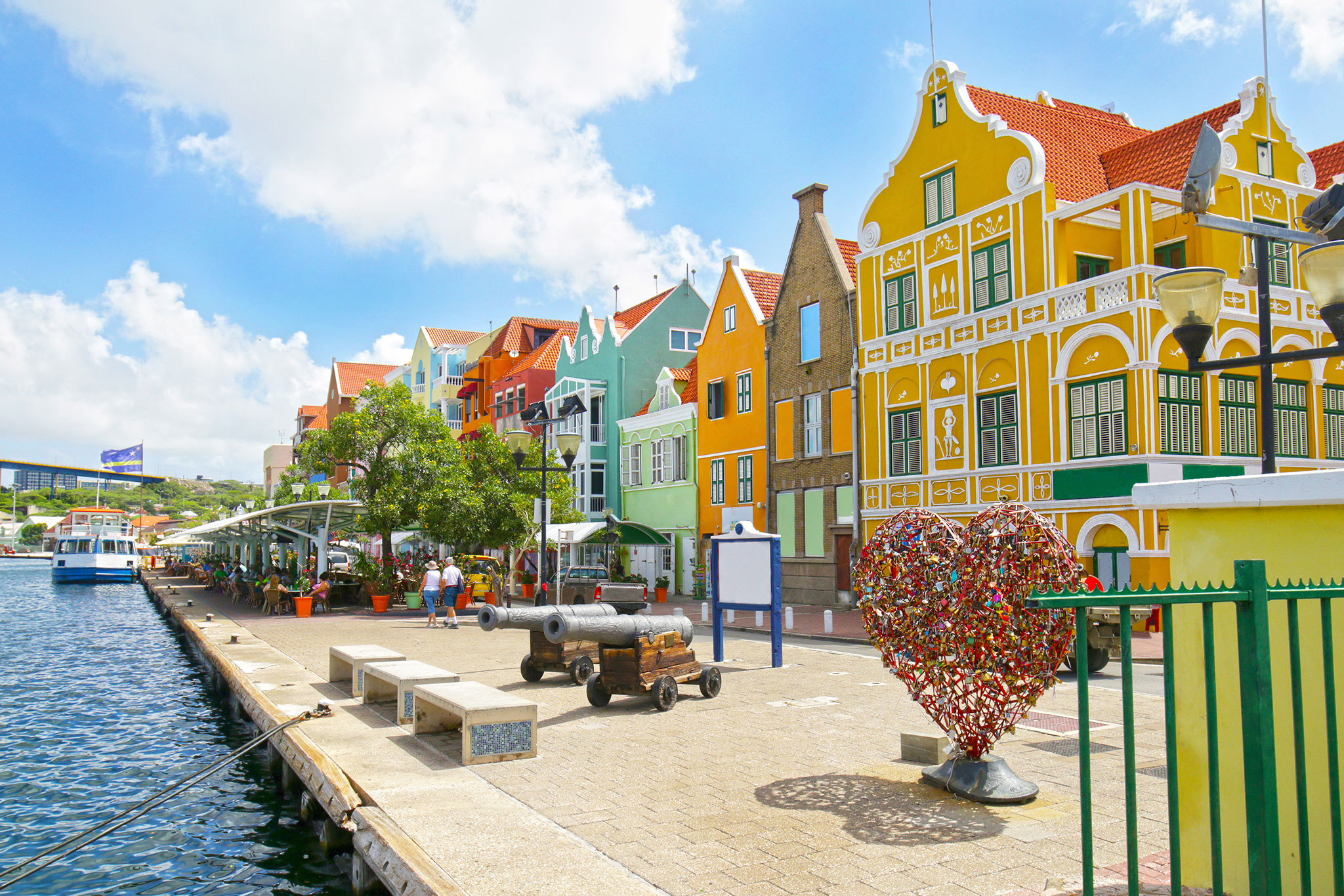 Brightly colored buildings line the Willemstad harbor with a lively outdoor market atmosphere.