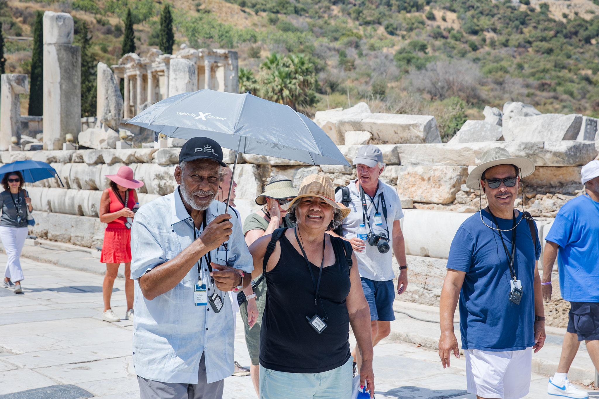 Christian travelers smiling and walking along a path lined with ancient ruins. Some people are holding umbrellas.