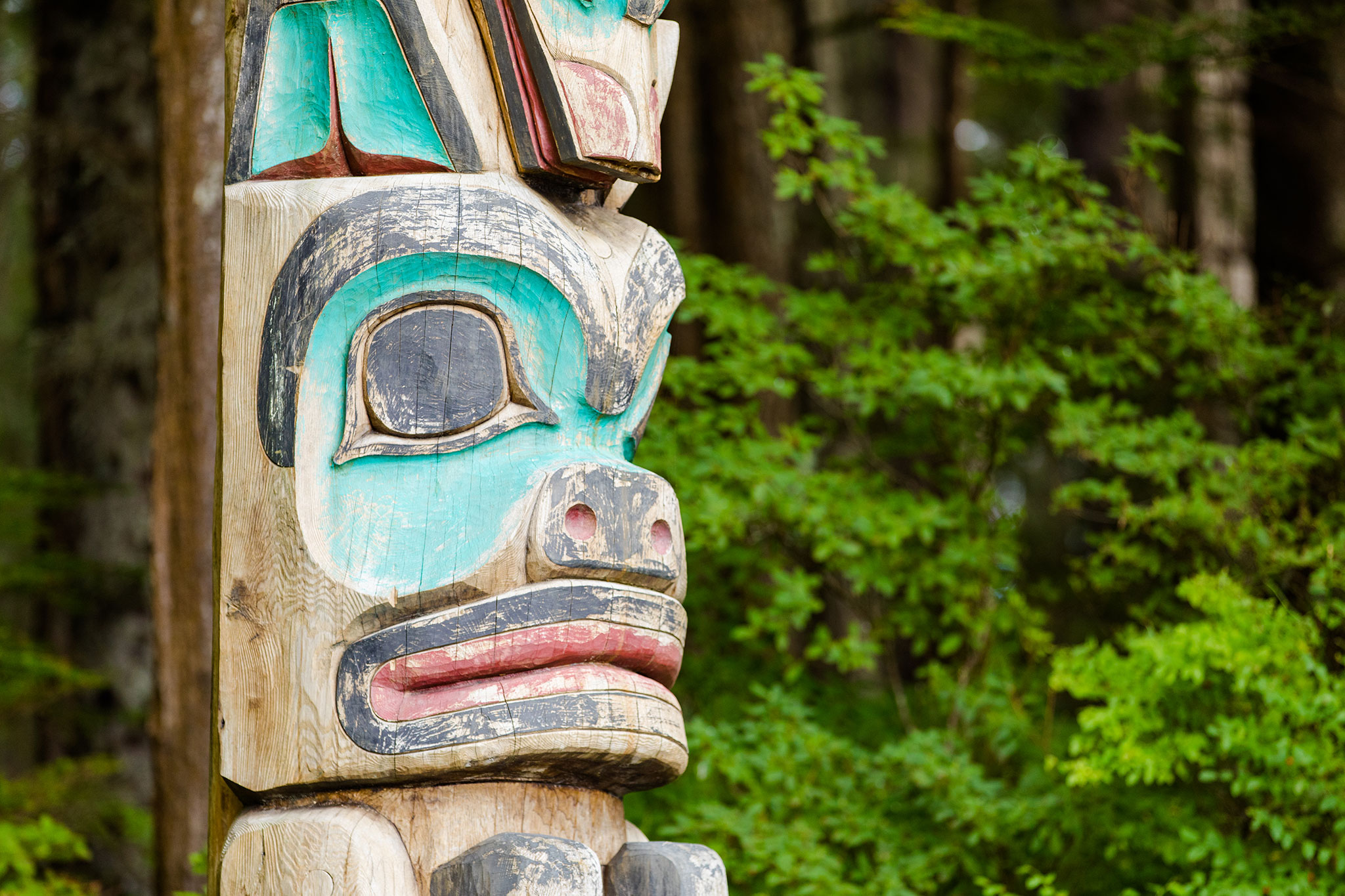 Detailed view of a totem pole featuring blue and red patterns among green trees.