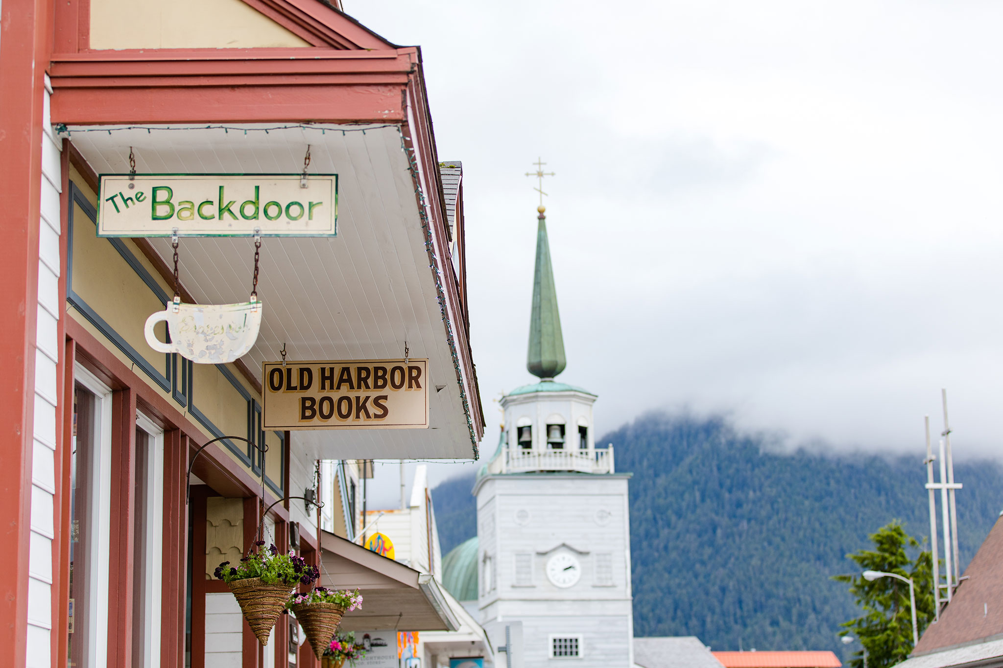 Colorful shop fronts on a cloudy day with a church spire and misty mountains in the background.