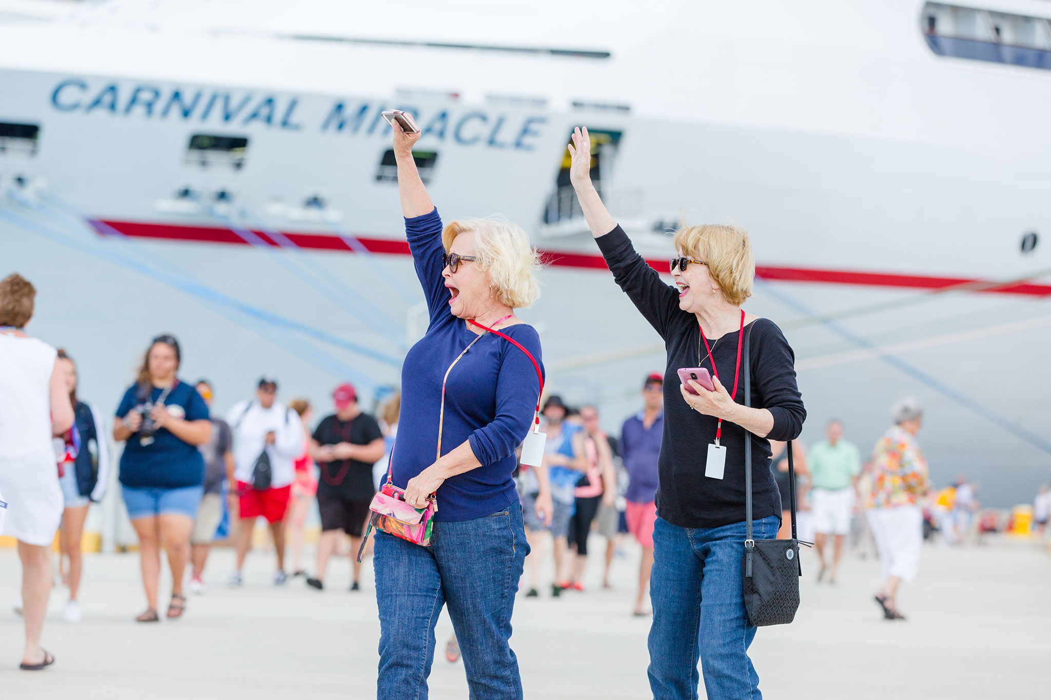 Joyful senior women excitedly waving in front of a cruise ship.