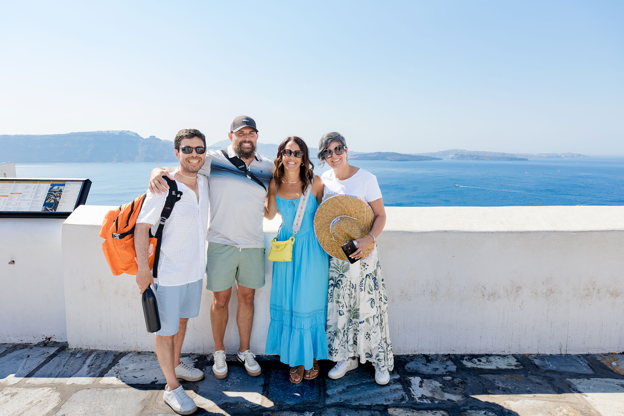 Group of two men and two women smiling together on a sunny day with the sea and cliffs in the background.