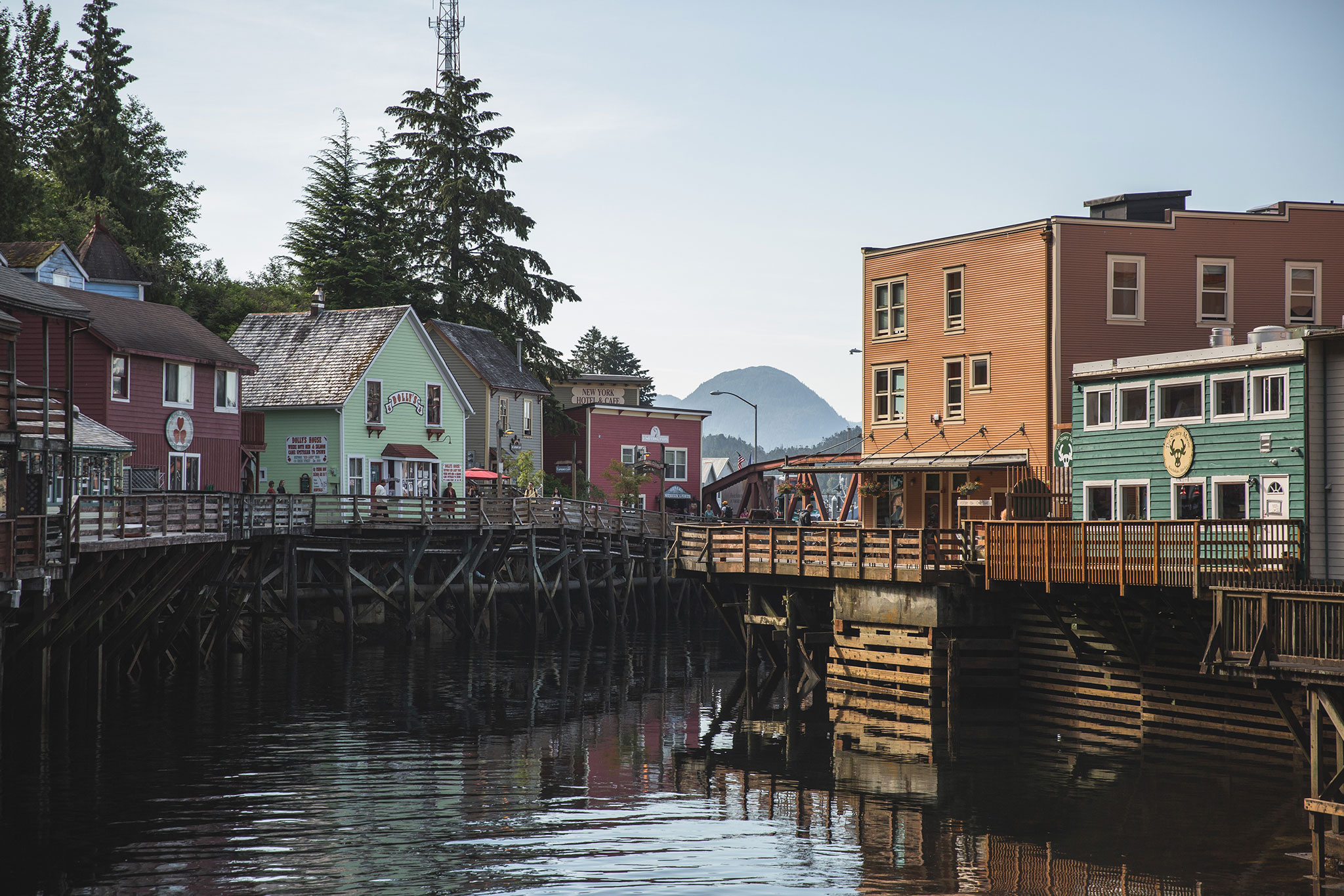 Quaint waterfront street with vibrant wooden buildings on stilts over a reflective river.