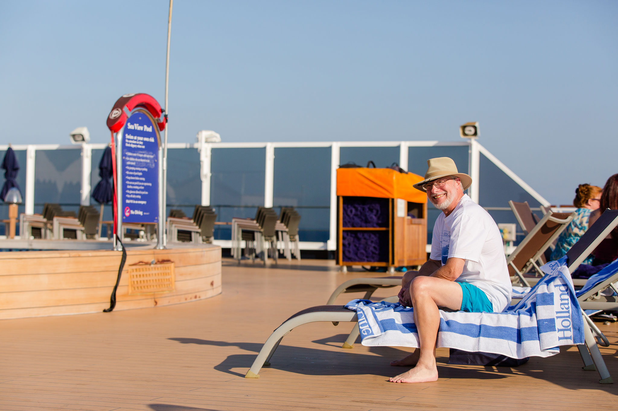 Happy senior male enjoying the sun on a deck chair aboard a cruise, sporting a casual outfit and a cheerful expression.