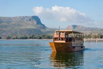 Scenic view of a Galilee boat, a replica of those from Jesus’ time, floating on calm waters with a flat-topped mountain in the distance.