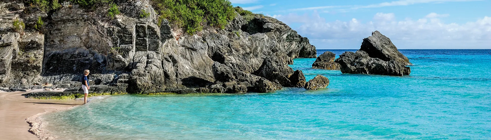 Woman standing on the shore, admiring the bright blue ocean and rocky landscape