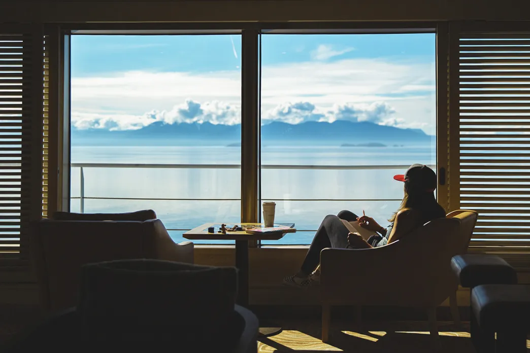 Woman sitting next to a window looking out at the snowcapped mountains of Alaska