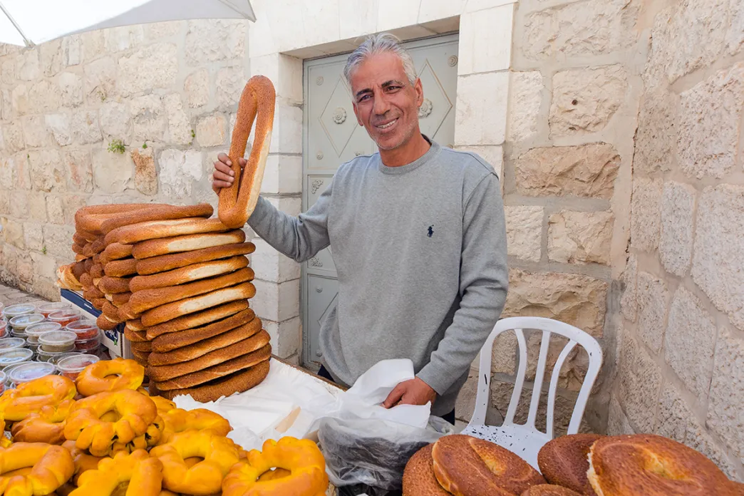 Man standing behind a table filled with different types of bread