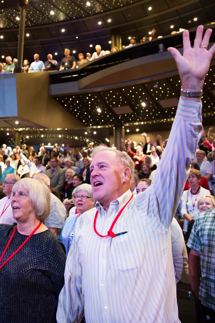 Man with a lifted hand singing in an auditorium filled with people