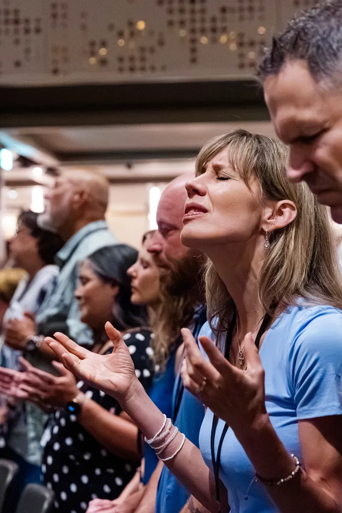 Woman standing with a group of people with eyes closed and hands raised