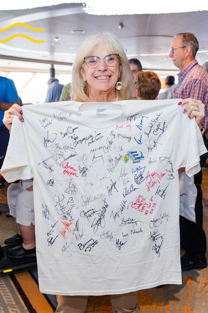 Smiling woman holding up a white t-shirt covered in colorful signatures