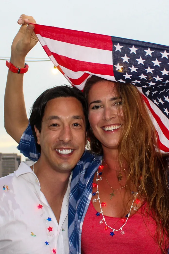 A couple standing together holding up an American flag behind them