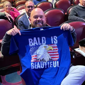 Man holding up a shirt with a Bald Eagle on it that says 