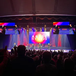 Singers on a colorful stage performing to an auditorium full of people